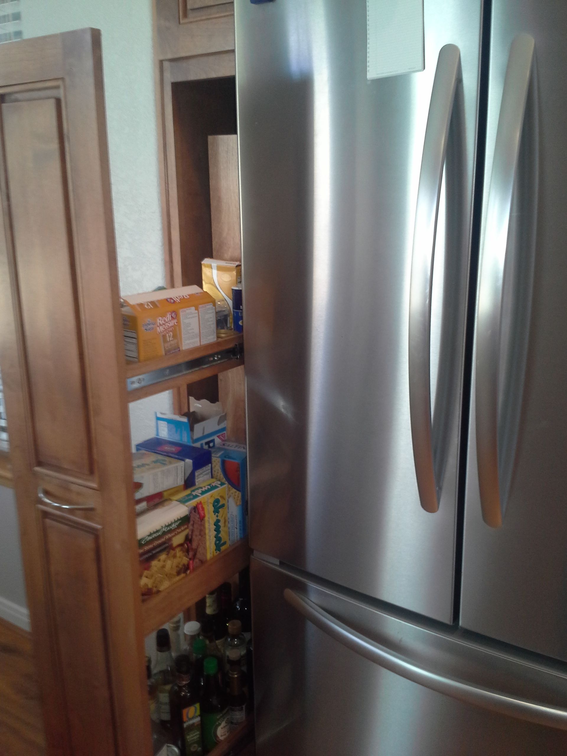 A stainless steel refrigerator in a kitchen next to a pantry