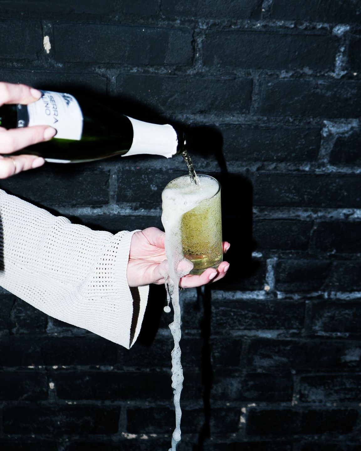 A woman's hands pour cava into an overflowing glass