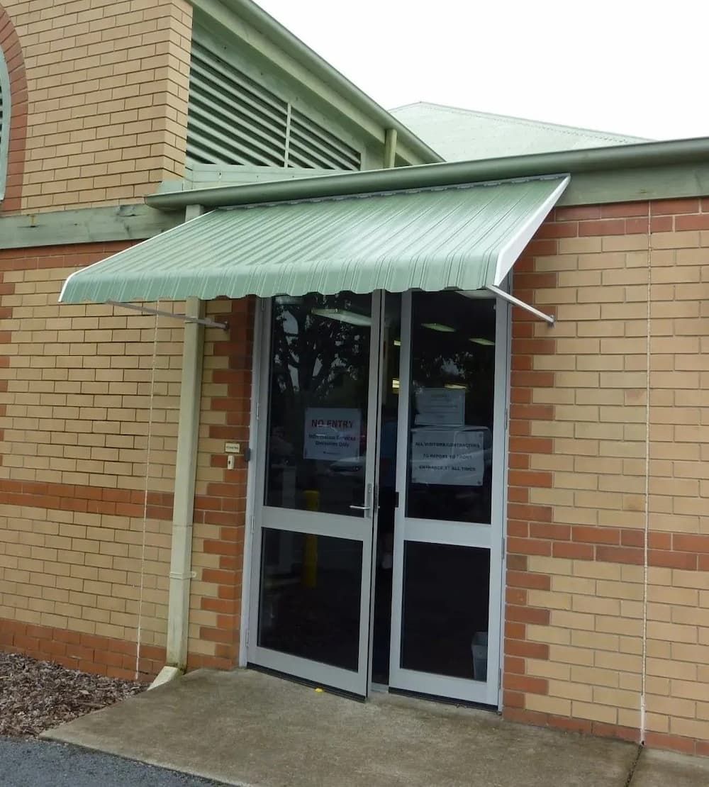 A Brick Building With A Green Awning Over The Door — Advantage Screens and Blinds Hervey Bay In Pialba, QLD