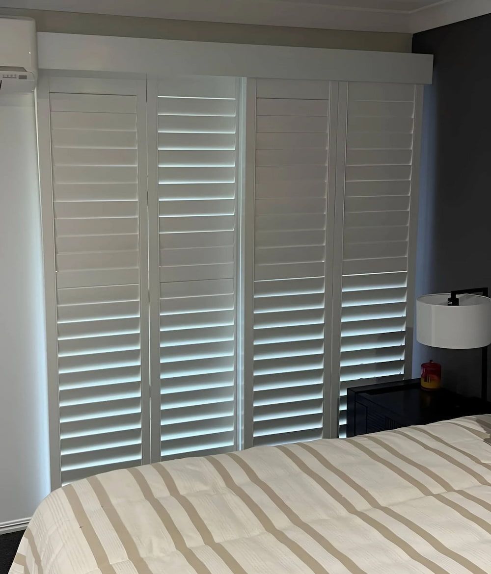 A Bedroom With A Bed And Shutters On The Windows — Advantage Screens and Blinds Hervey Bay In Pialba, QLD