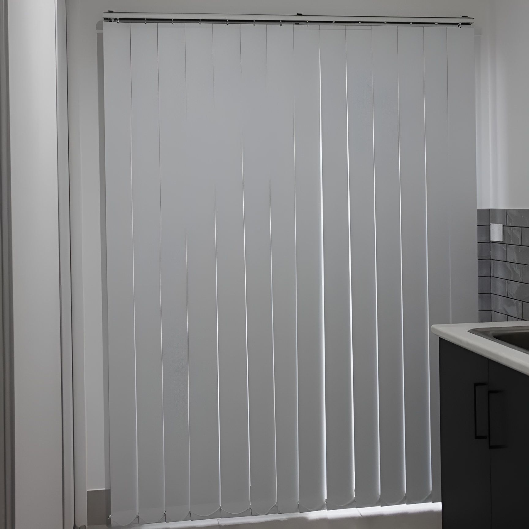 A White Vertical Blind Is Hanging On A Window In A Kitchen — Advantage Screens and Blinds Hervey Bay In Pialba, QLD