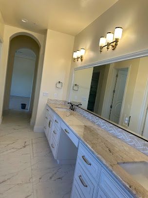 Bathroom with white cabinets, marble countertop, large mirror, and three light fixtures.