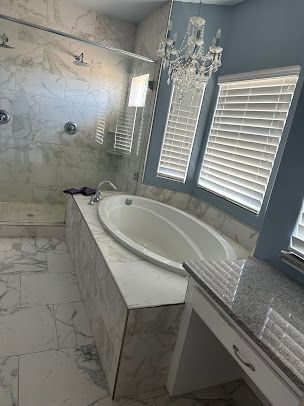 Bathroom with a white oval bathtub, marble tiles, and a chandelier.