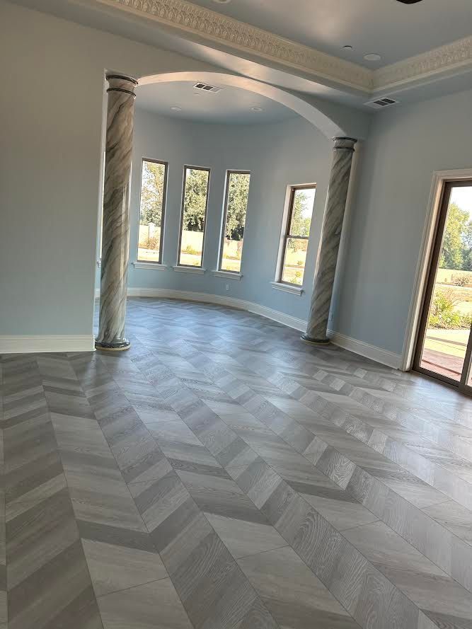 Spacious room with herringbone pattern floor, light blue walls, arched columns, and large windows.