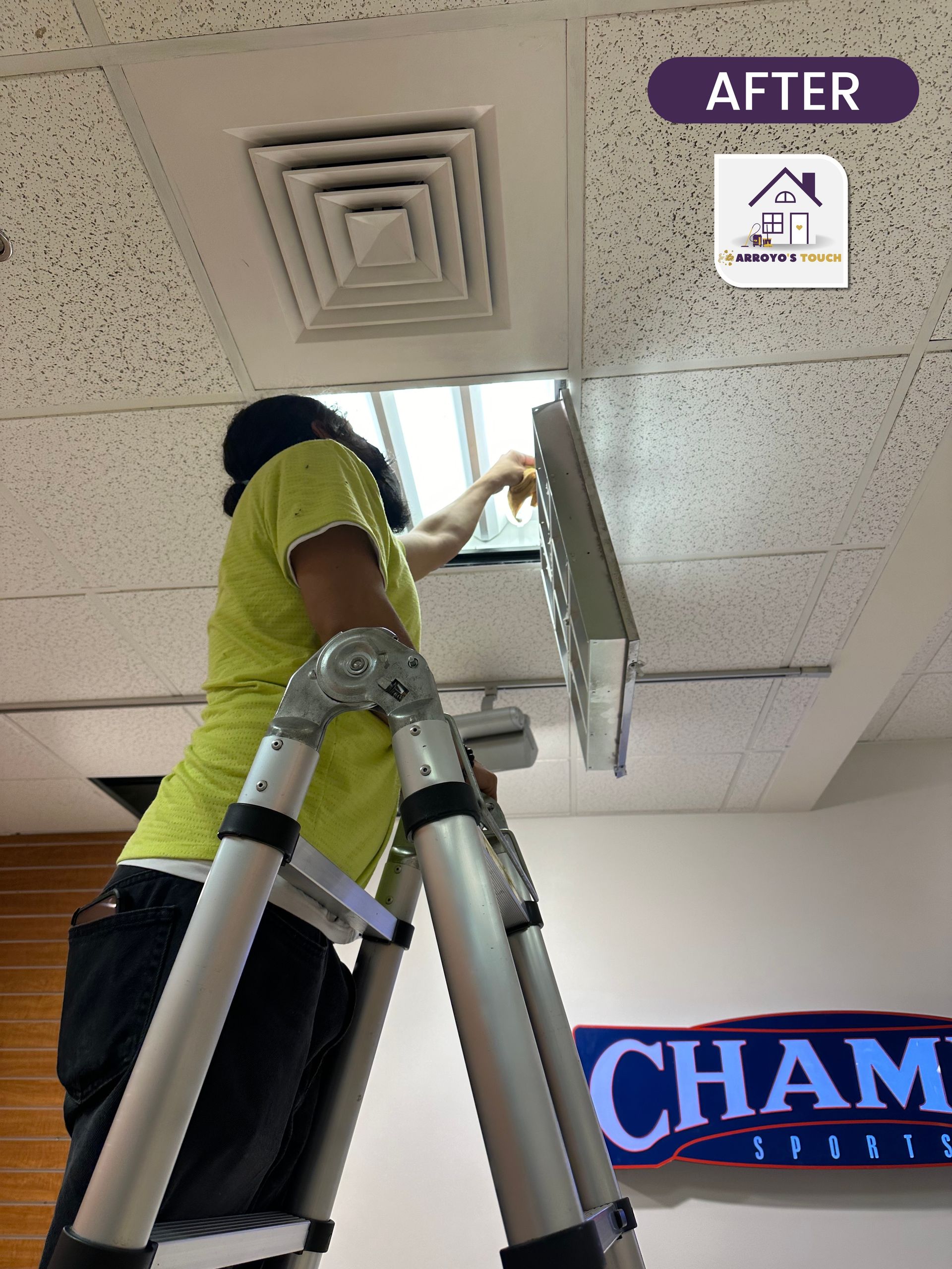 Person on a ladder cleaning an air vent in a commercial setting;