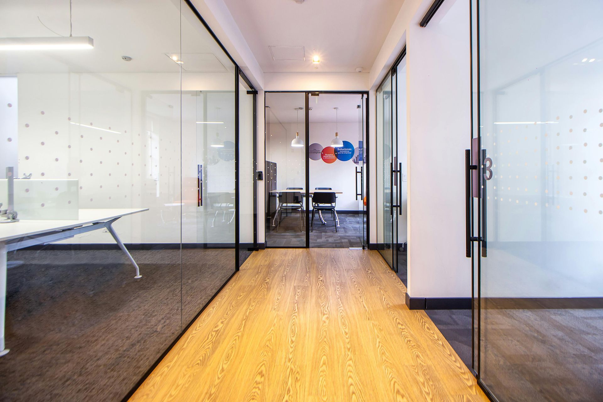 Office hallway with glass walls, wooden floor, and office spaces visible.