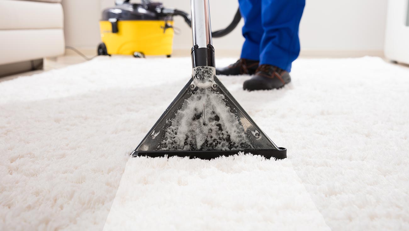 Person in blue pants vacuuming white carpet with a yellow vacuum in the background.