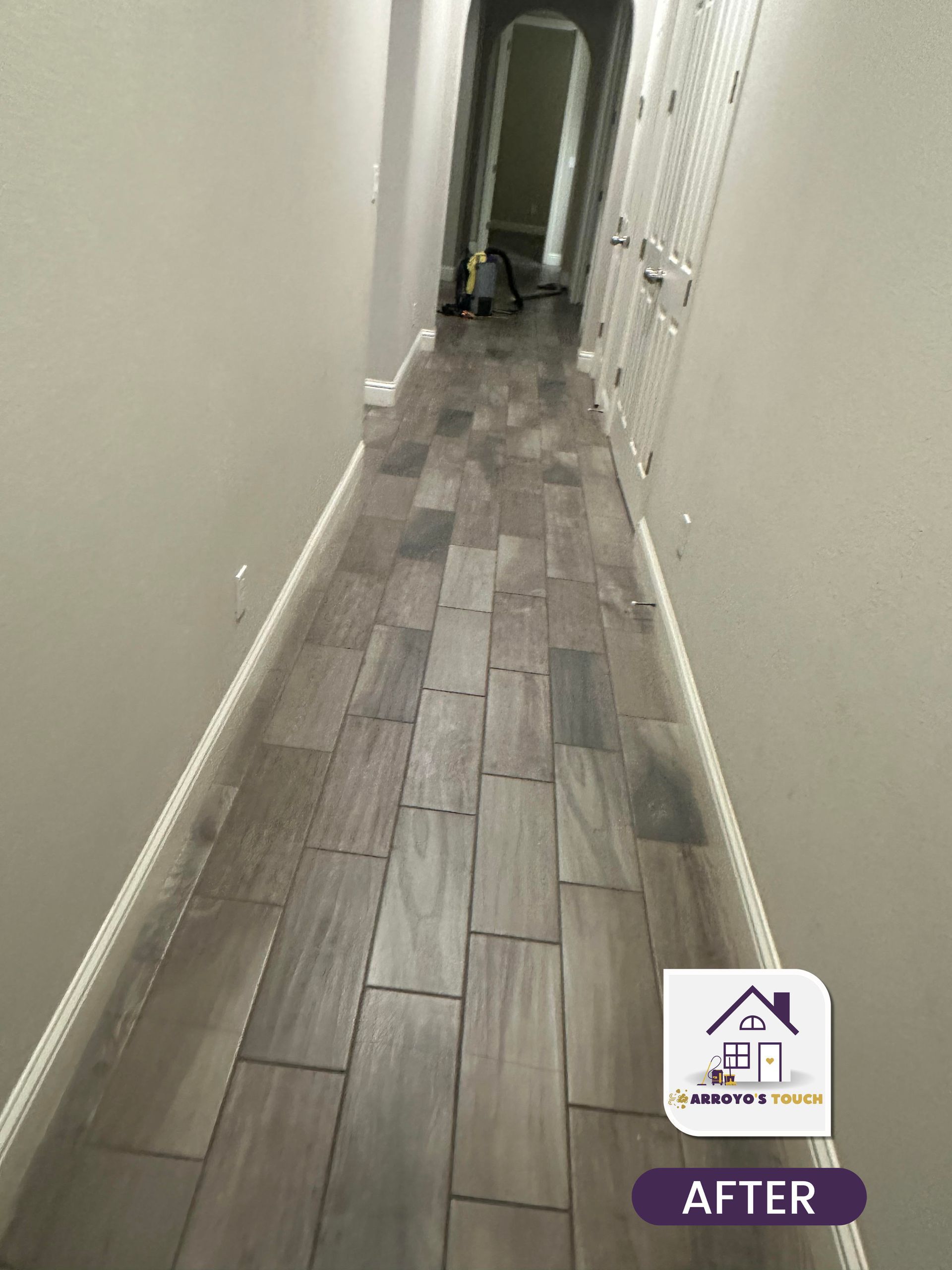 Long hallway with gray wood-look tile flooring, white trim and light gray walls. 