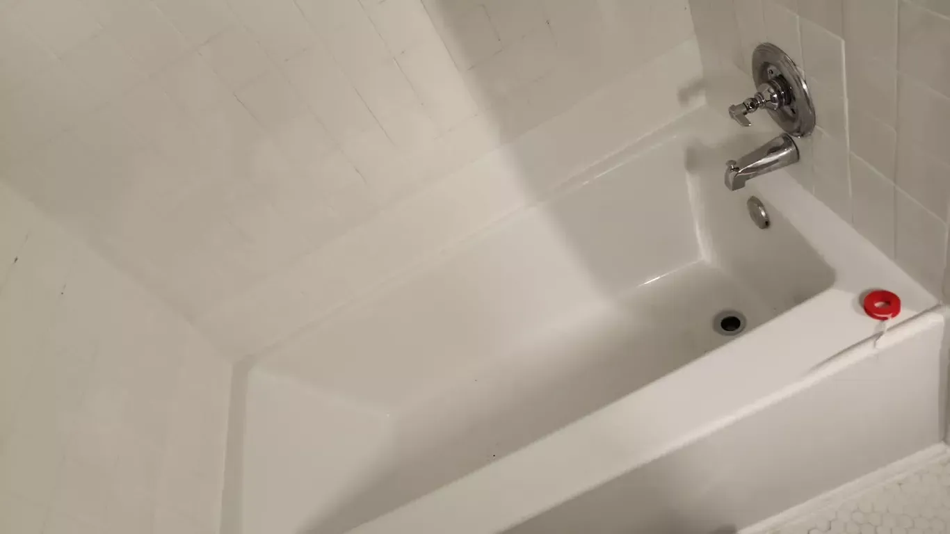 A white bathtub with a red ball on the edge of it.