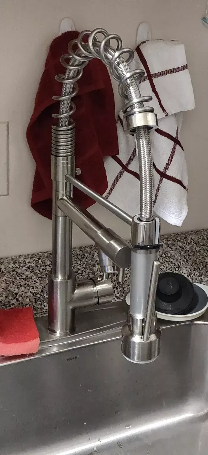 A kitchen sink with a faucet and towels hanging on the wall.