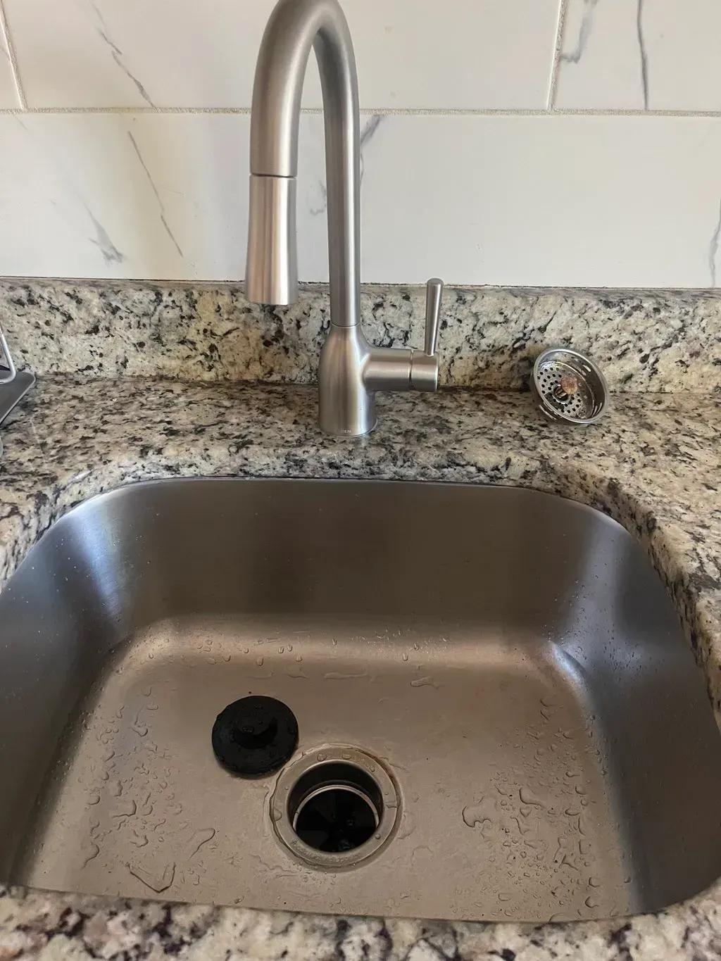 A stainless steel kitchen sink with a faucet on a granite counter top.