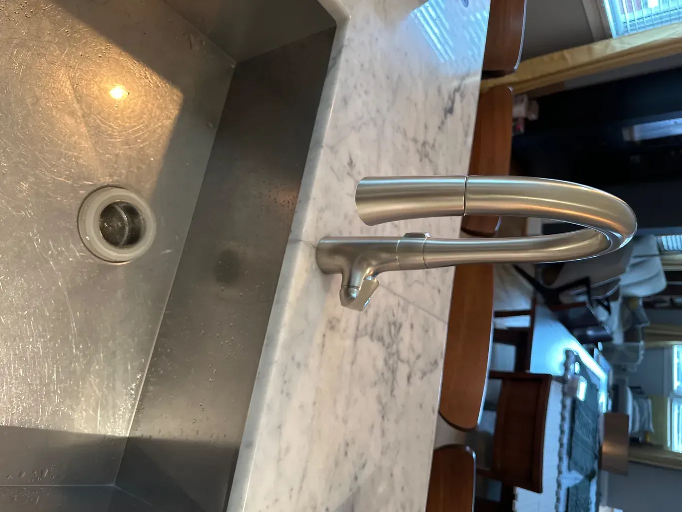 A kitchen sink with a stainless steel faucet on a marble counter top.