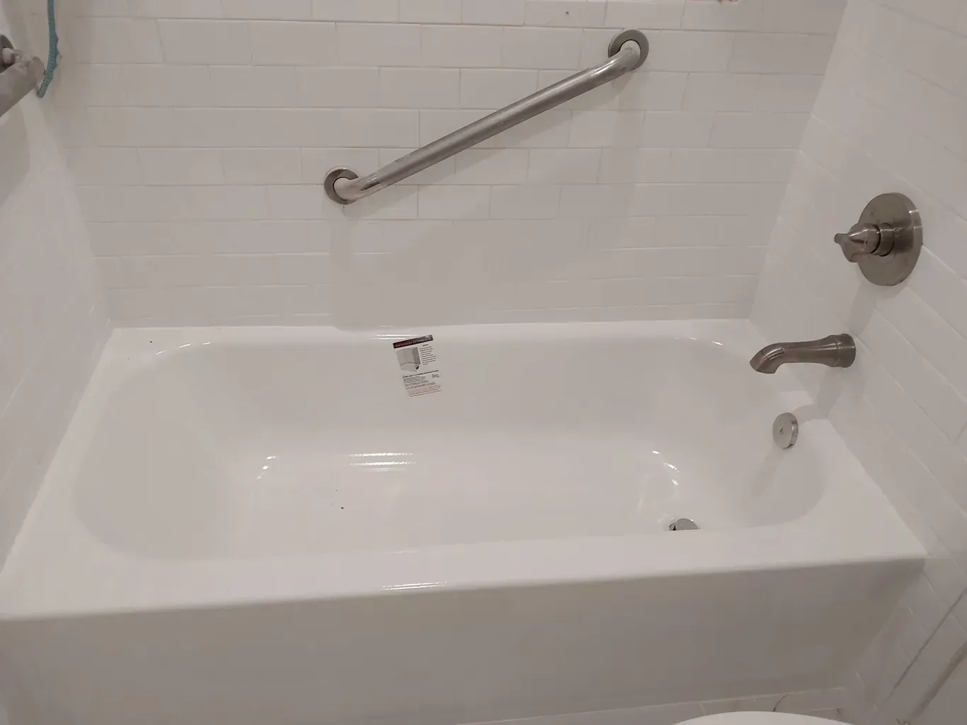 A white bathtub with a stainless steel railing in a bathroom next to a toilet.