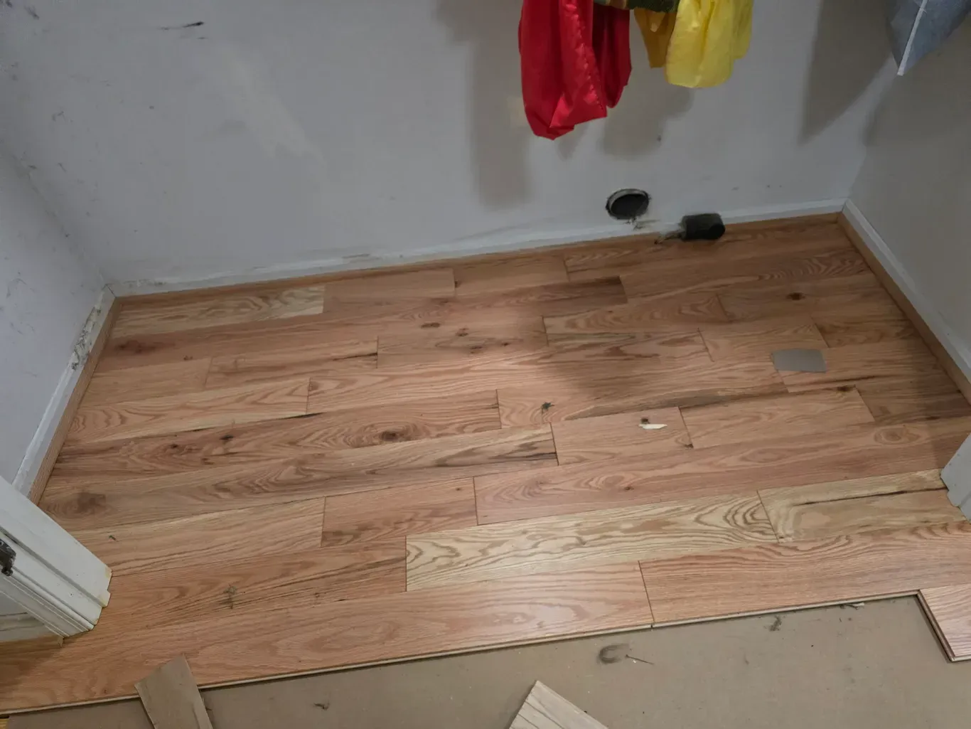A wooden floor in a room with clothes hanging on the wall.