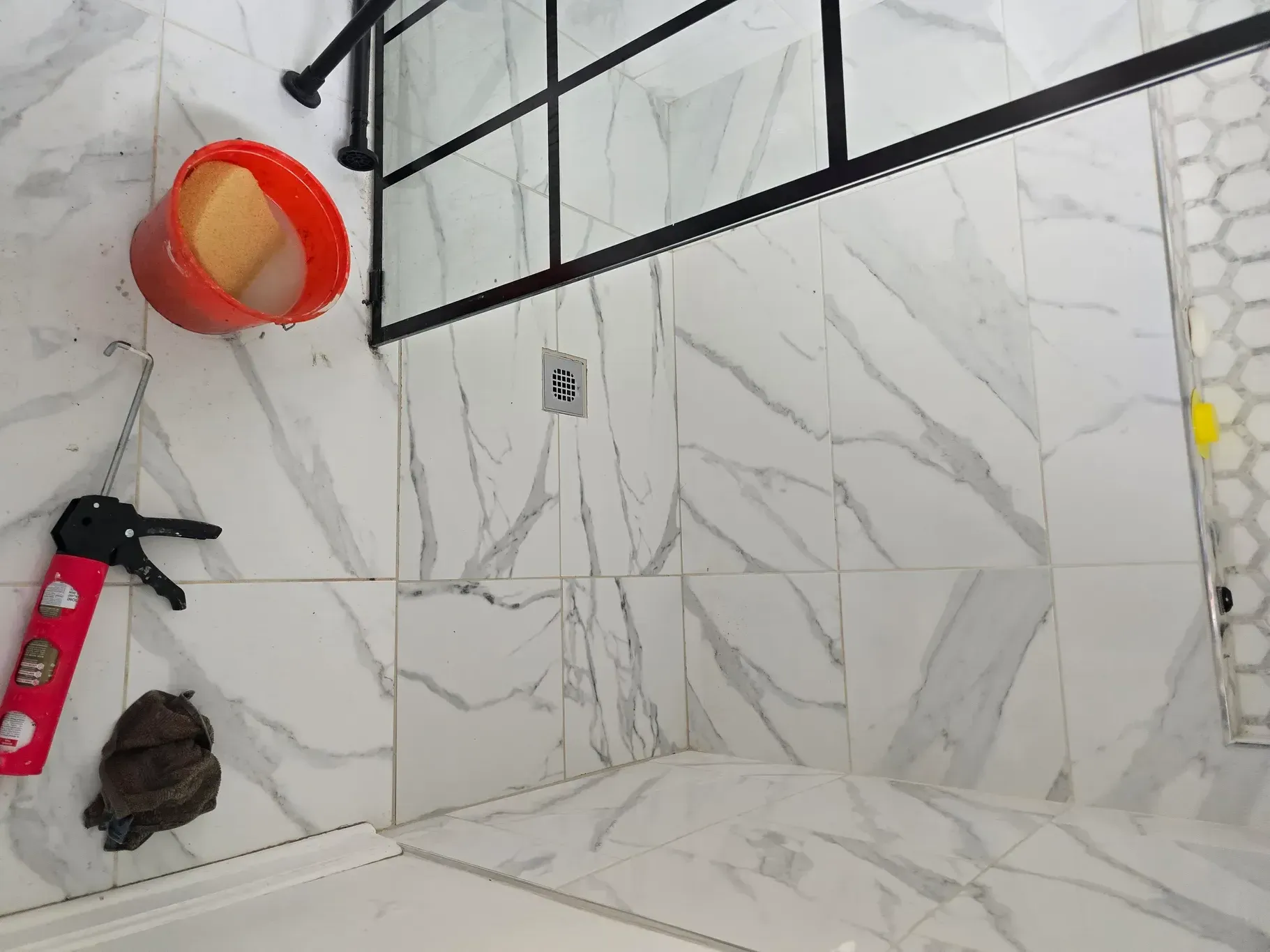 A bathroom with white tiles and a red bucket on the floor.