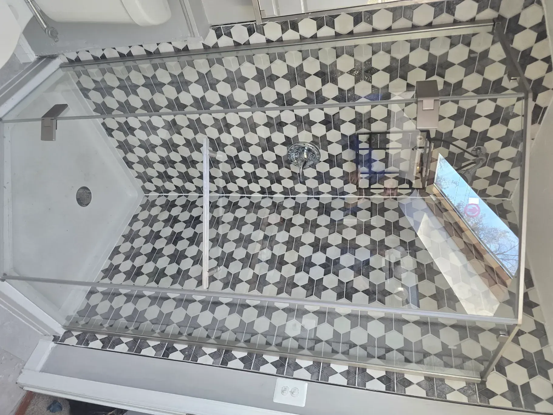 A bathroom with a walk in shower with a black and white tile wall.