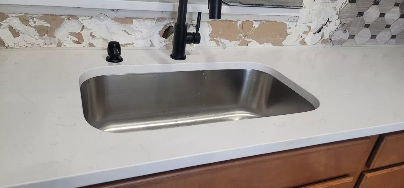 A stainless steel kitchen sink with a black faucet on a white counter top.
