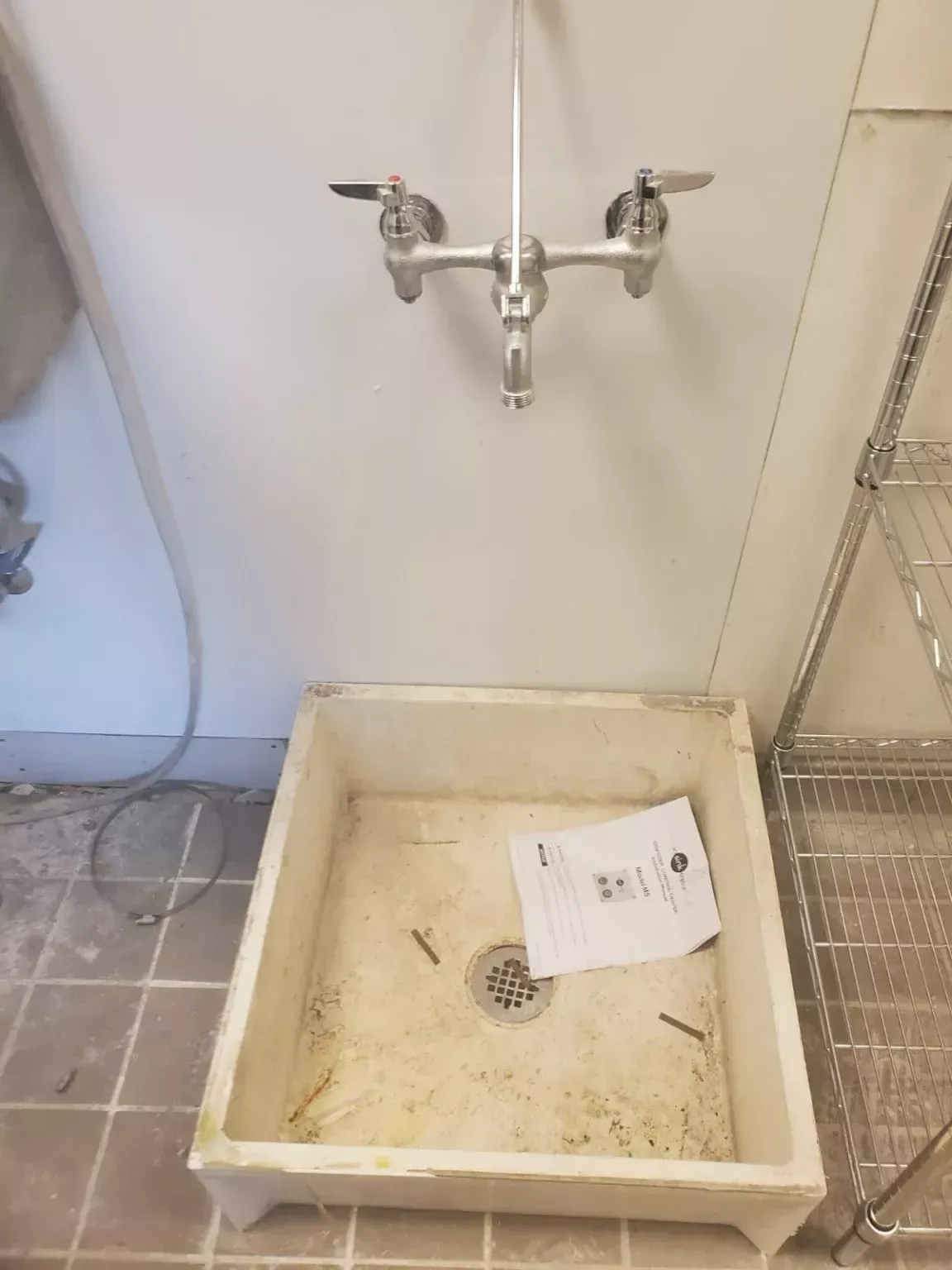 A bathroom sink with a faucet and a paper on the floor.