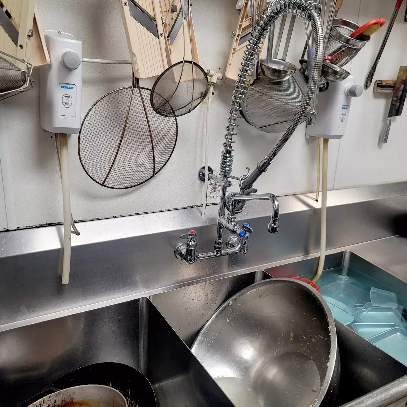 A kitchen sink with a faucet and utensils hanging on the wall.