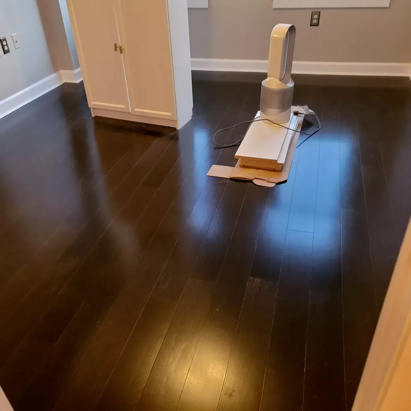 A room with hardwood floors and a fan on the floor.