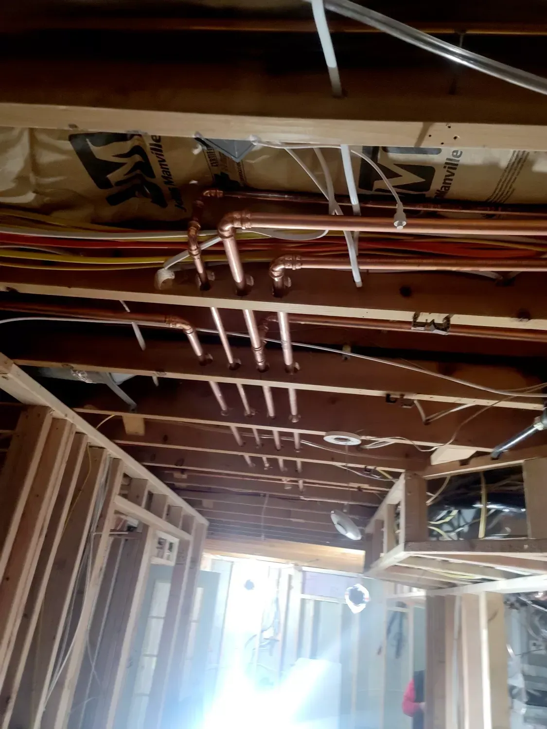 The ceiling of a building under construction with pipes and wires hanging from it.