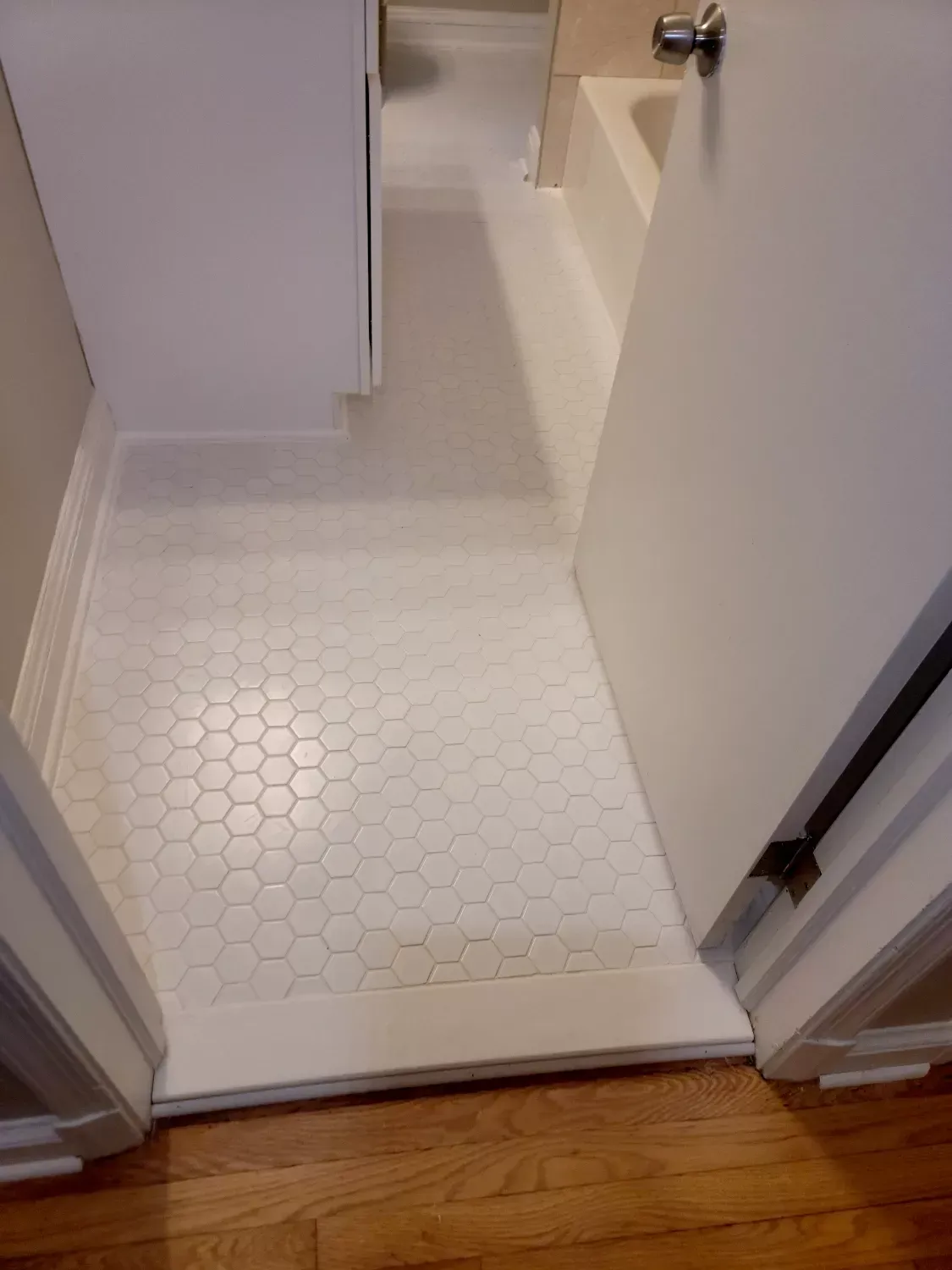 A bathroom with a white tile floor and a wooden floor.
