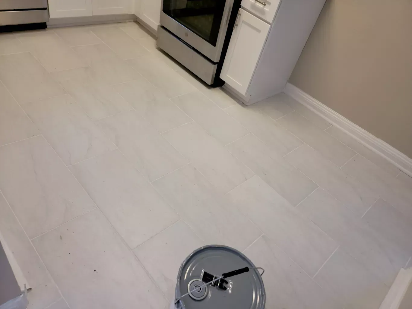 A bucket of paint is sitting on the floor of a kitchen.
