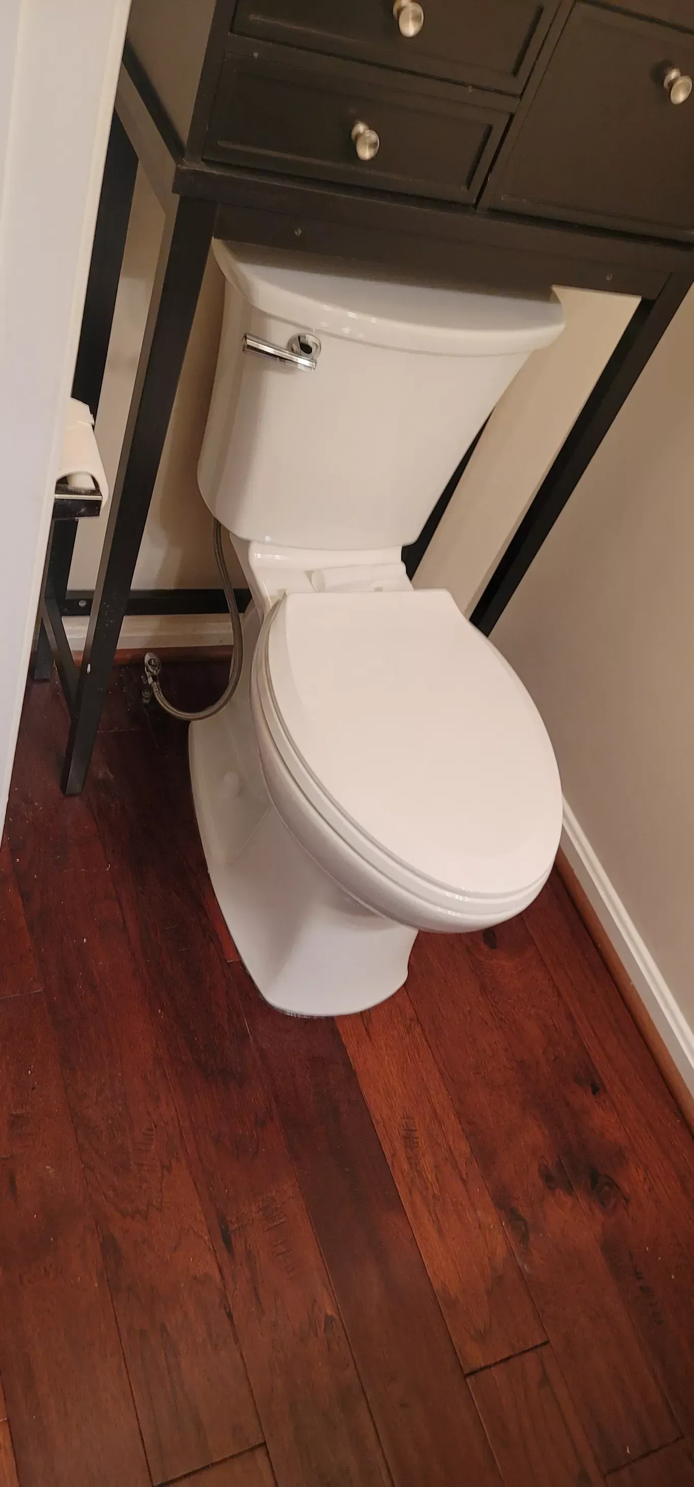 A white toilet is sitting on a wooden floor next to a black dresser.