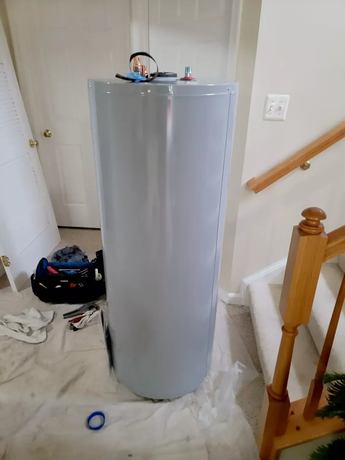 A large white water heater is sitting on the floor next to a staircase.