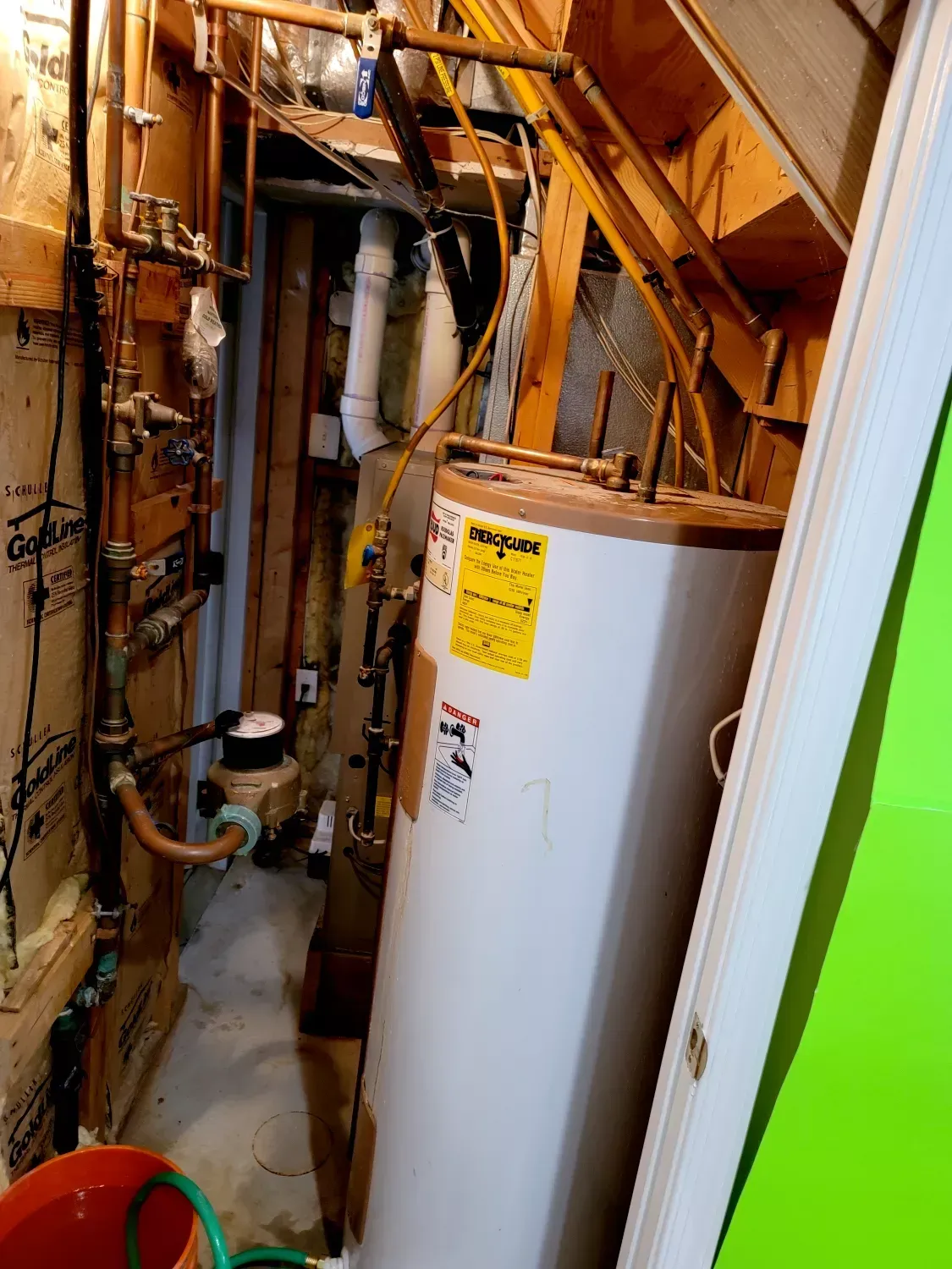 A water heater is sitting in a basement next to stairs.