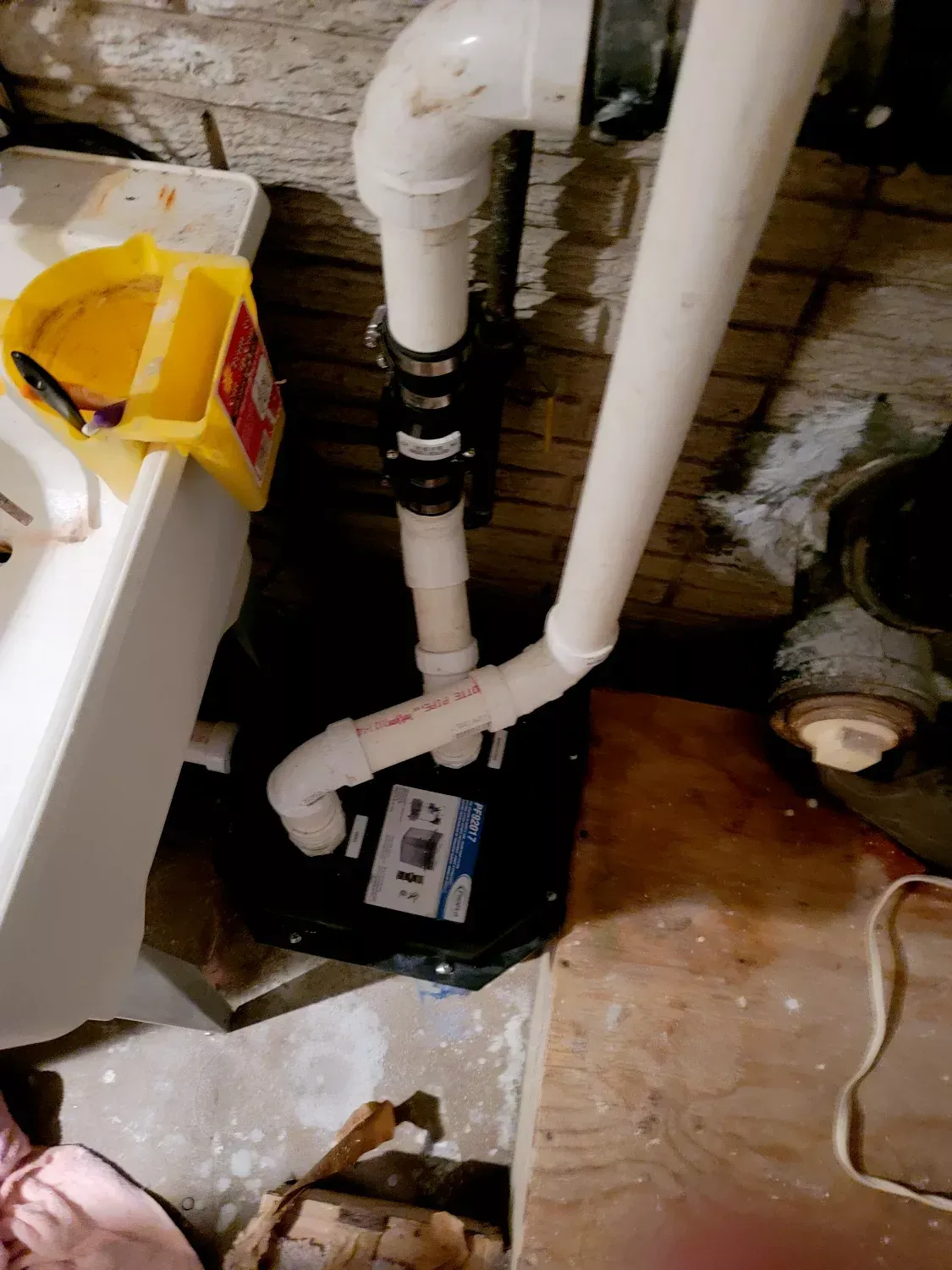 A drain pump is sitting in a basement next to a sink.