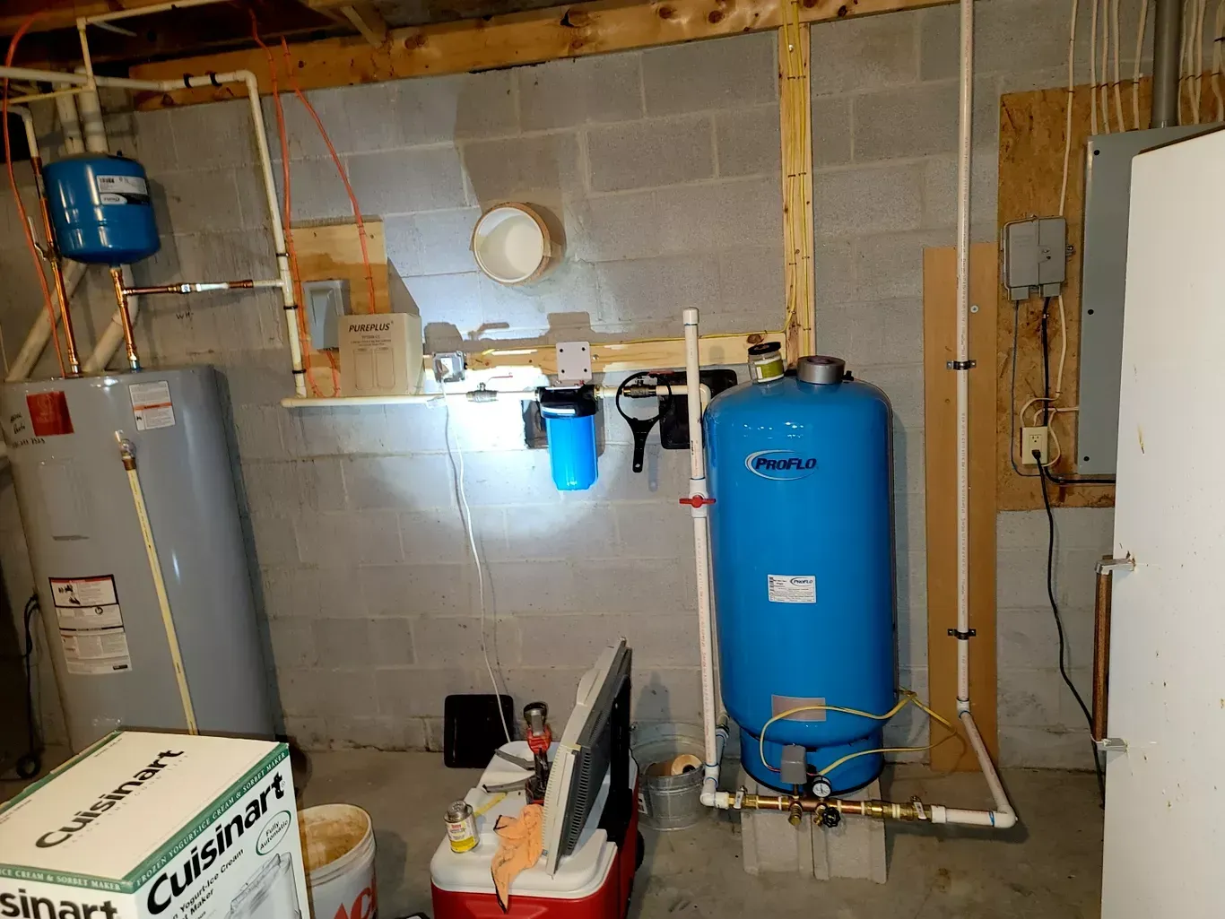 A blue water tank is sitting in a basement next to a water heater.