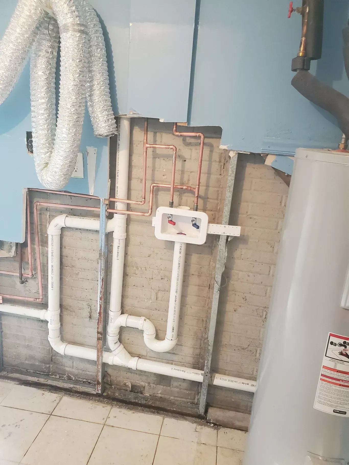 A room with a water heater and pipes on the wall.