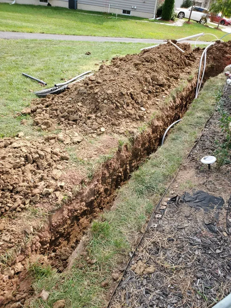 A trench is being dug in the grass in front of a house.
