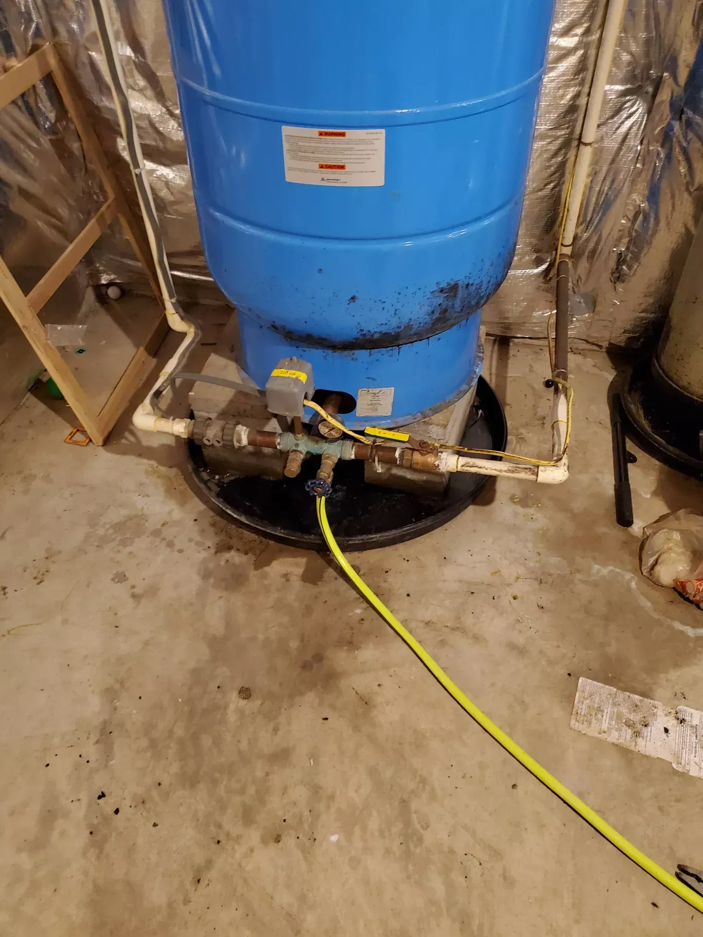 A blue water tank with a yellow hose attached to it is in a basement.