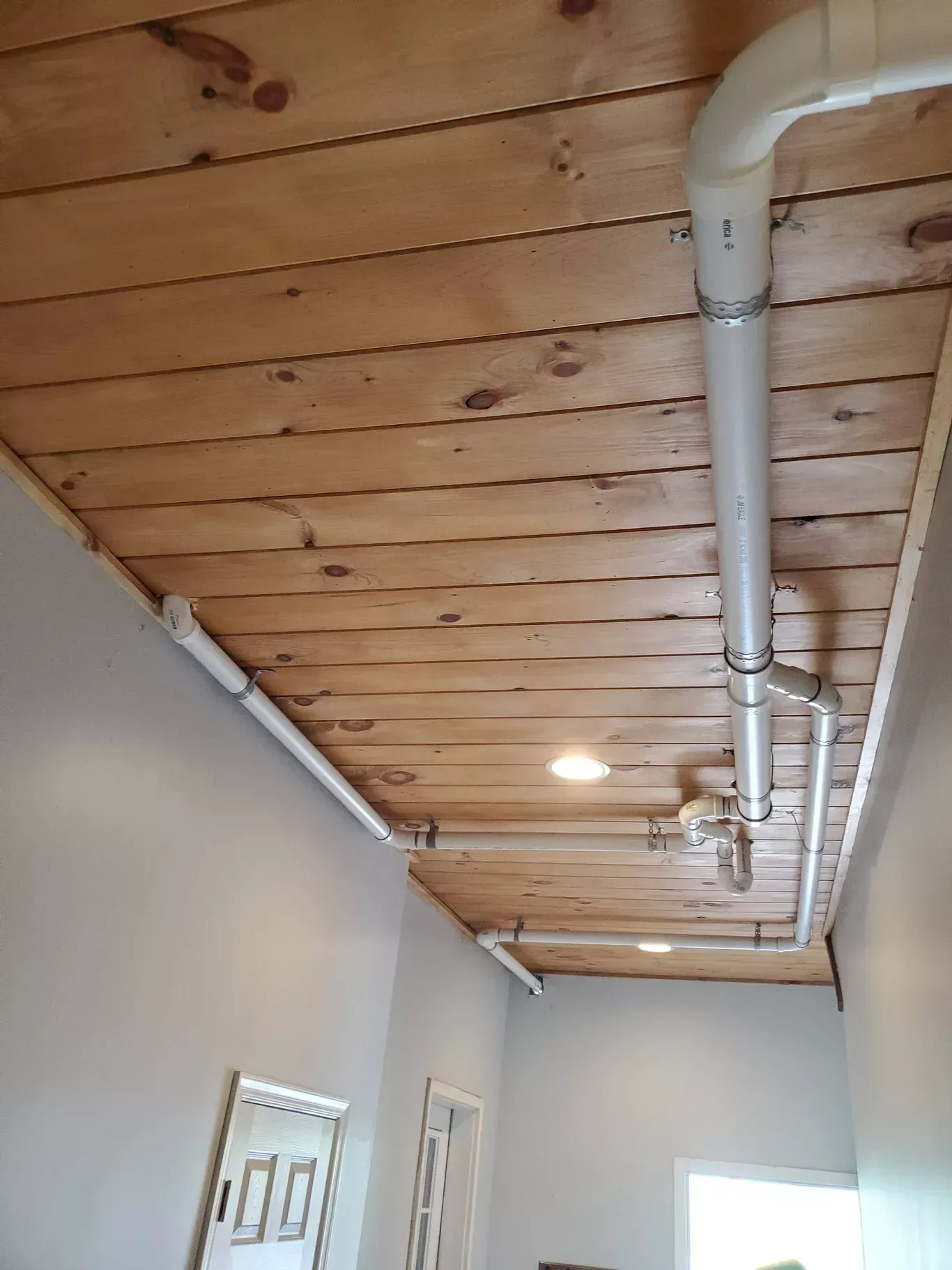 A hallway with a wooden ceiling and white pipes.