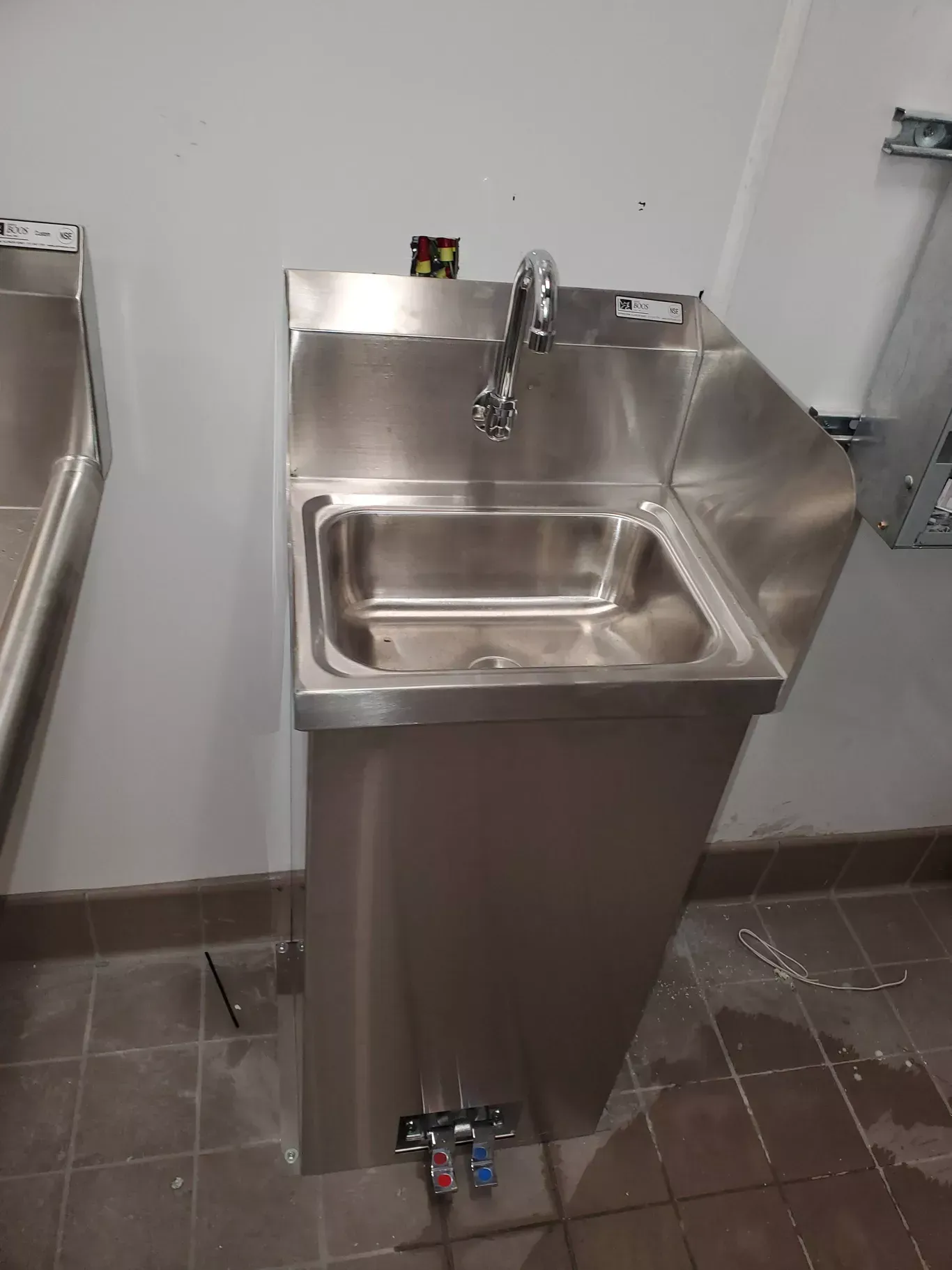 A stainless steel sink is sitting on a tiled floor in a bathroom.