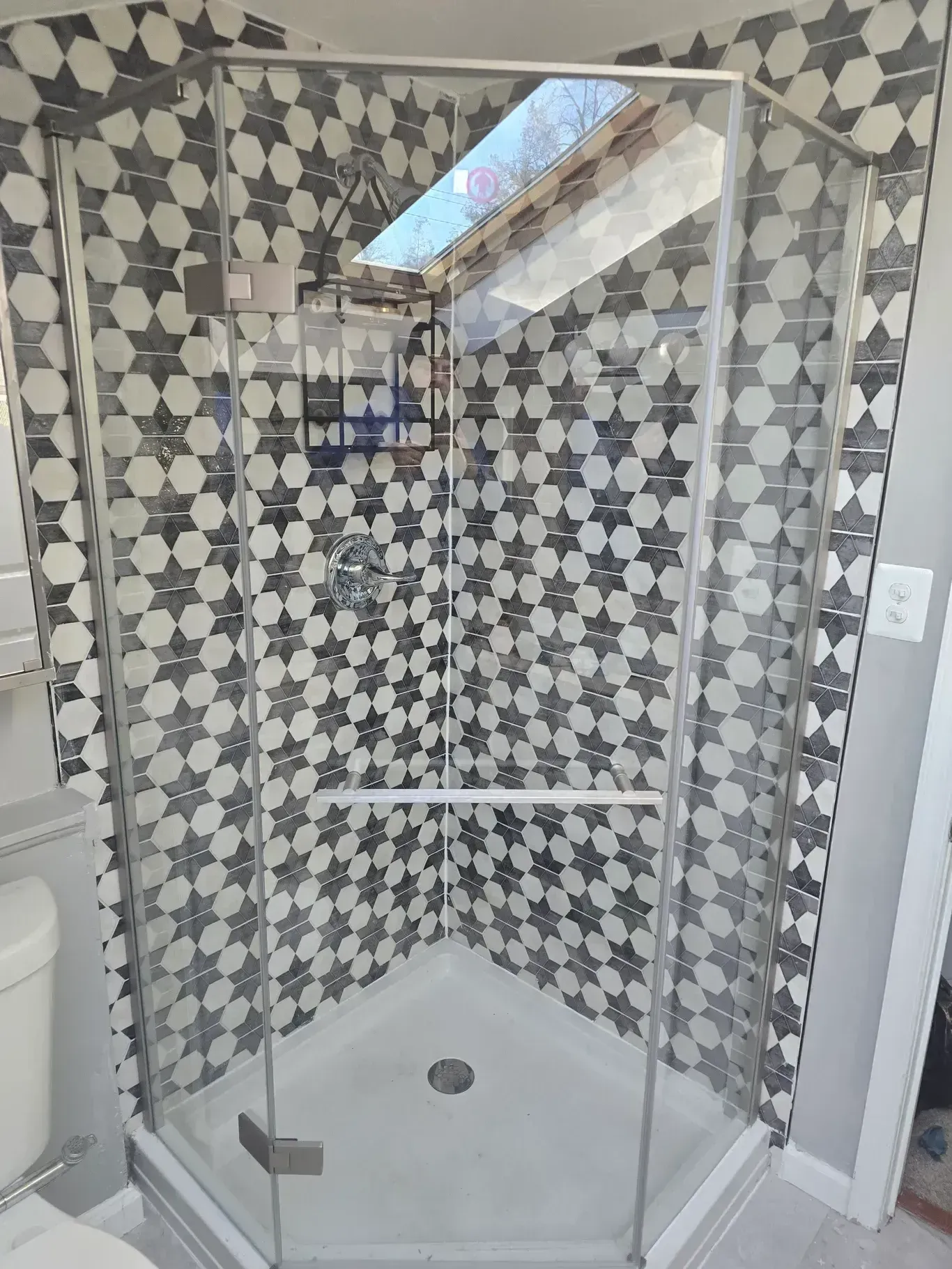 A bathroom with a walk in shower with a black and white tile wall.