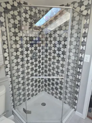 A bathroom with a walk in shower with a black and white tile wall.