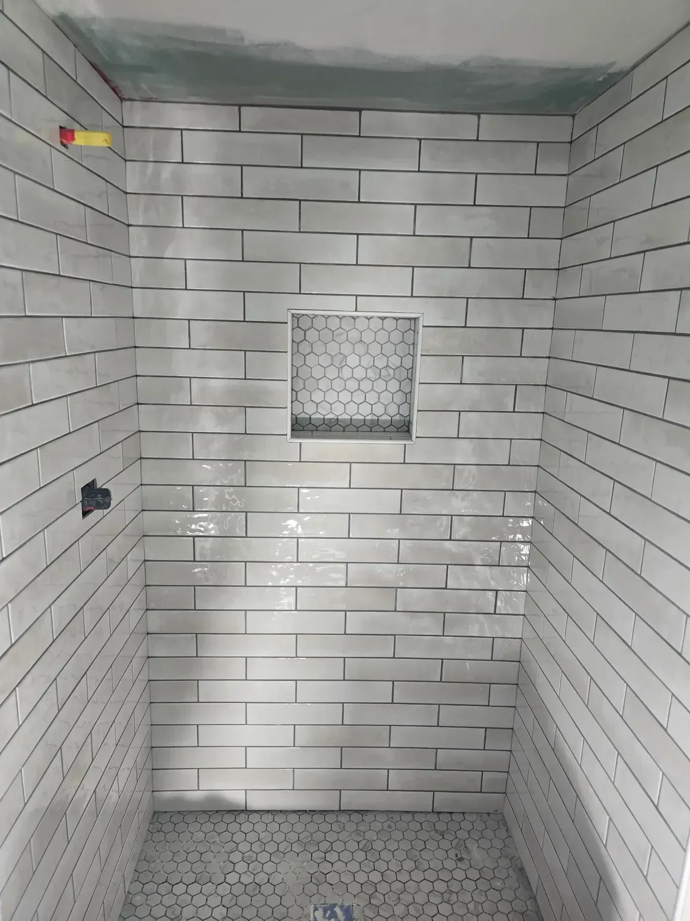 Shower stall with light gray brick-like tiles and a small recessed shelf.