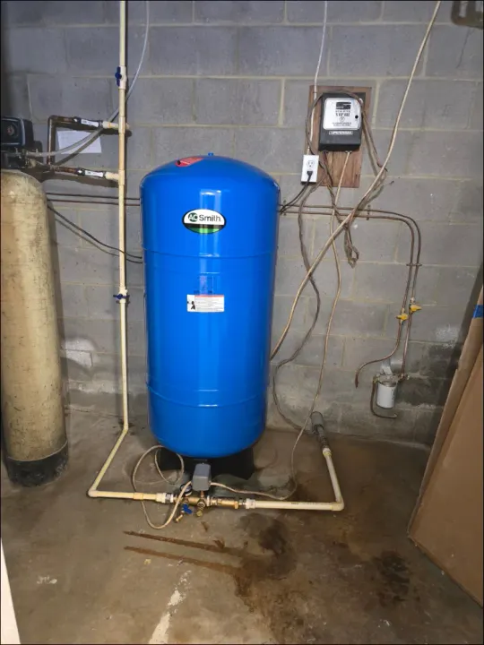 A blue water tank is sitting in a basement next to a brick wall.