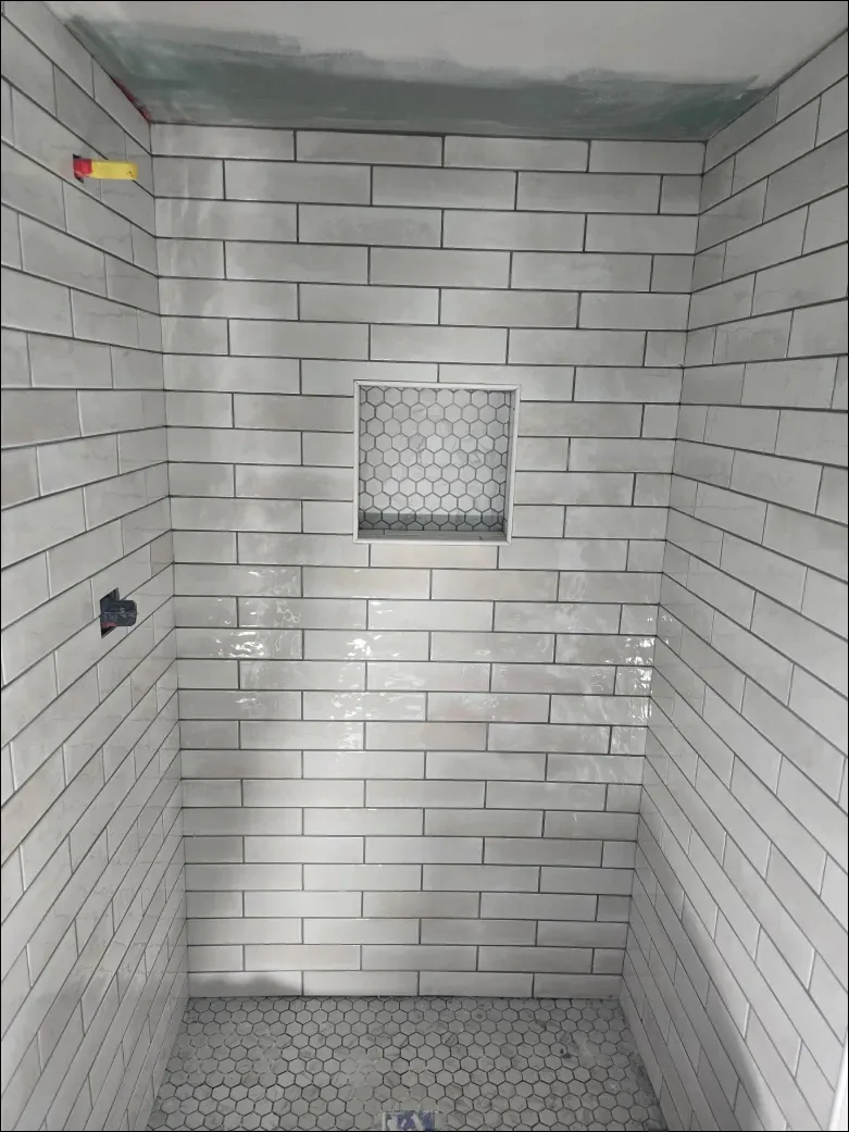 A shower stall with white tiles and a niche in the wall.