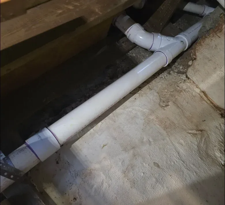 A white pipe is connected to a concrete wall