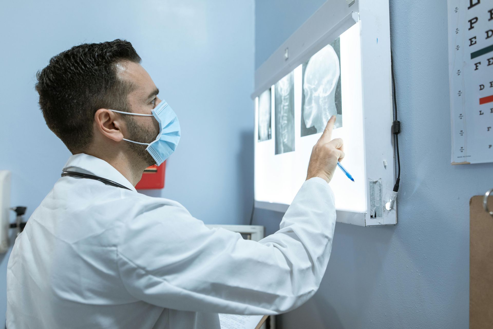 Doctor in mask examining X-ray on light board in a medical office.
