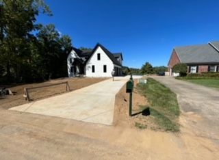 A white house is sitting on the side of a dirt road next to a mailbox.