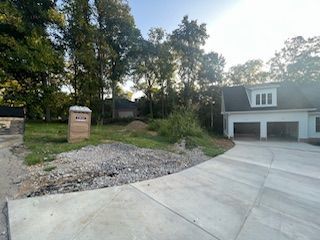 A concrete driveway leading to a house with a garage and trees in the background.
