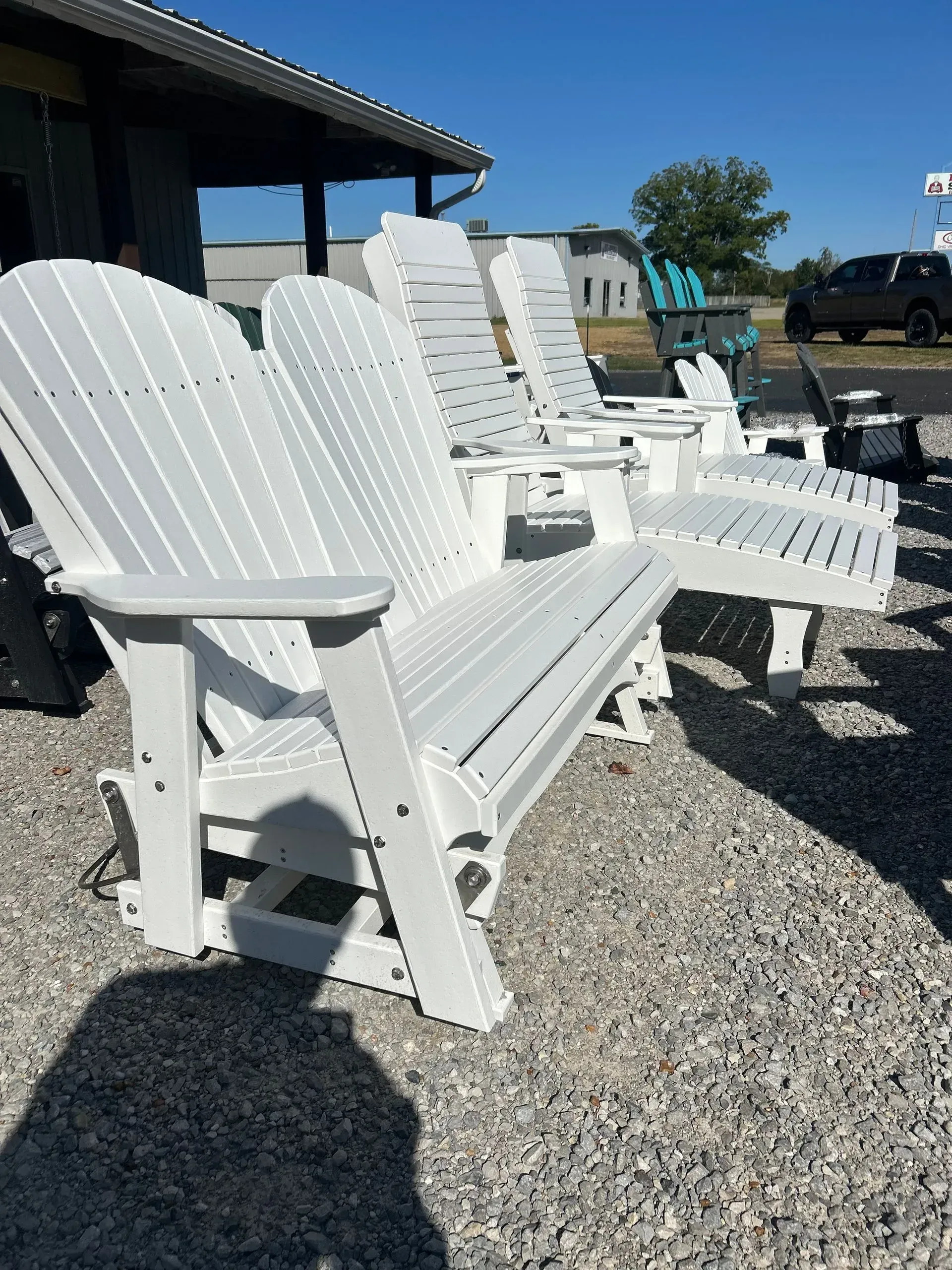 White outdoor glider bench set on a gravel surface under a blue sky.
