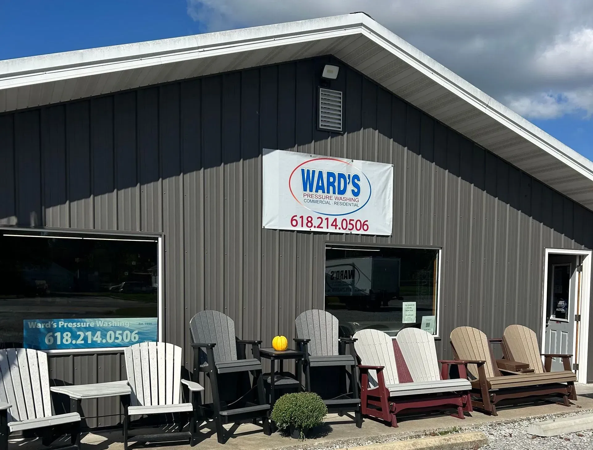 Gray building with a sign for Ward's, outdoor furniture display, blue and white sign, chairs lined up out front, and phone number.