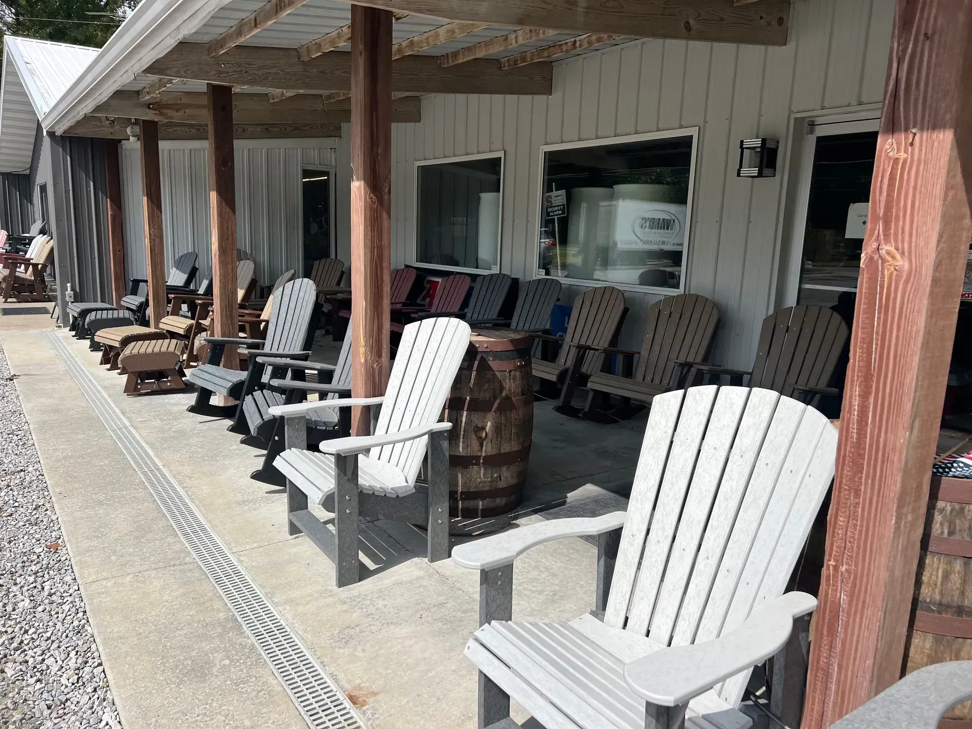 Chairs line the porch of a building with a white facade; barrels and stone path are visible.