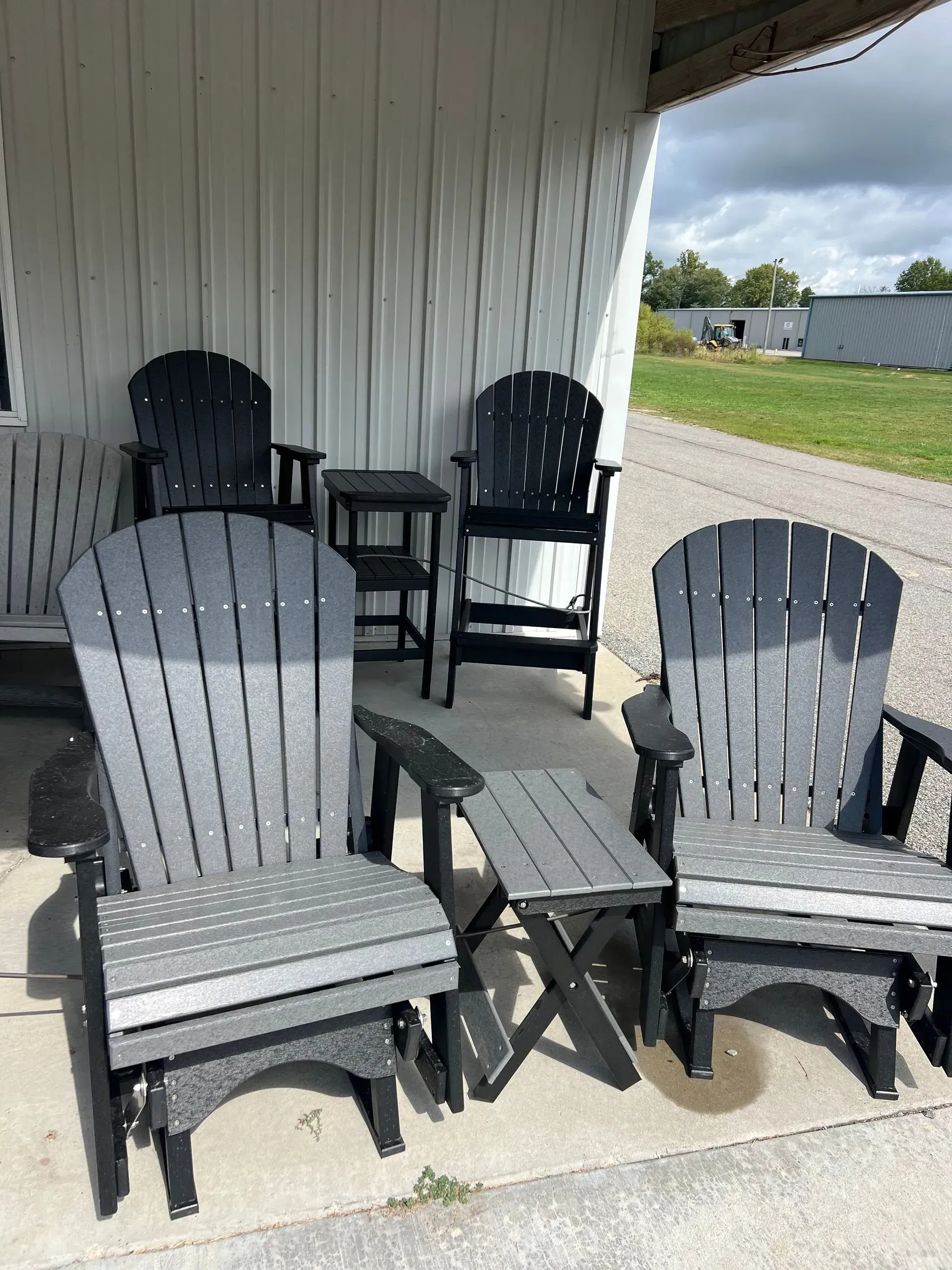 Outdoor furniture set: black and gray Adirondack chairs and side tables on a concrete surface.